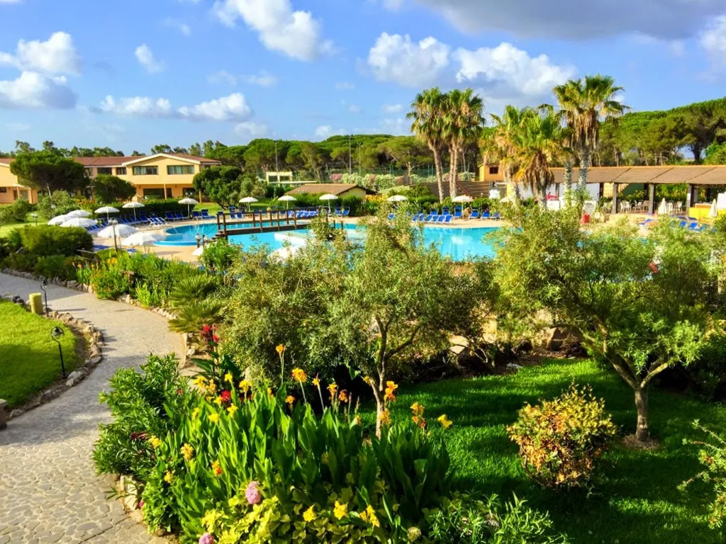 Giardino fiorito con vialetto che conduce alla piscina tra palme e vegetazione rigogliosa