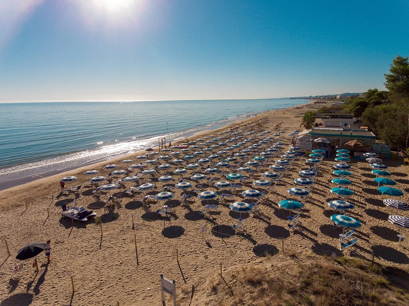 Spiaggia sabbiosa al tramonto con file di ombrelloni azzurri e bianchi e mare calmo