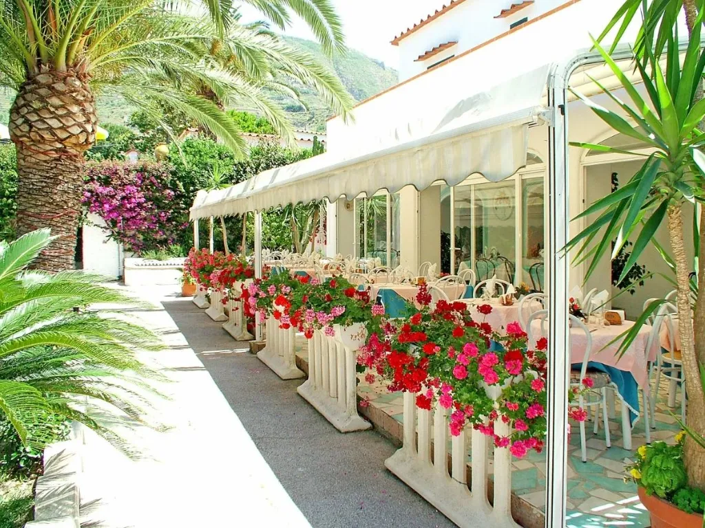 Terrazza ristorante coperta con fioriere di gerani rossi e palme lungo il vialetto