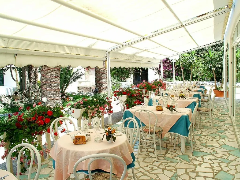 Ristorante esterno coperto da tenda con tavoli apparecchiati e fioriere di gerani