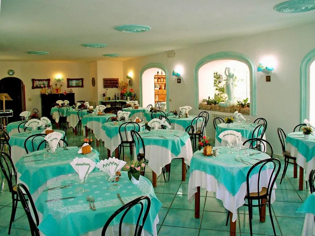 Sala ristorante interna con tavoli apparecchiati con tovaglie color acquamarina e sedie nere