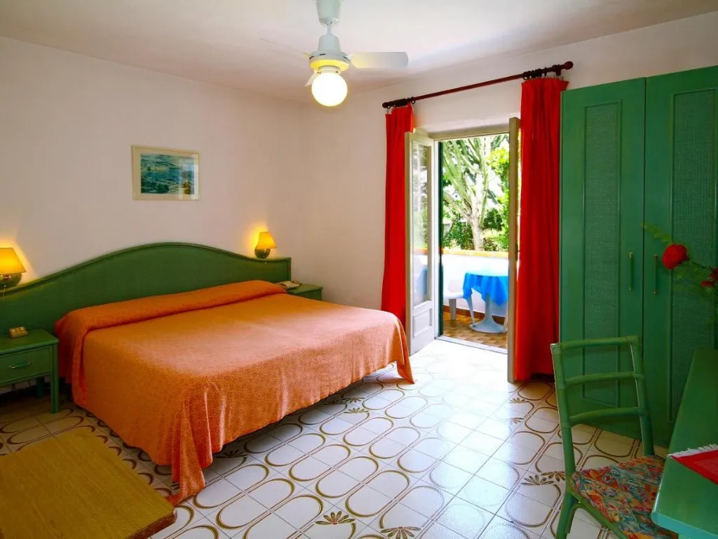 Camera da letto con letto matrimoniale, testiera verde, copriletto arancione e uscita sul terrazzo