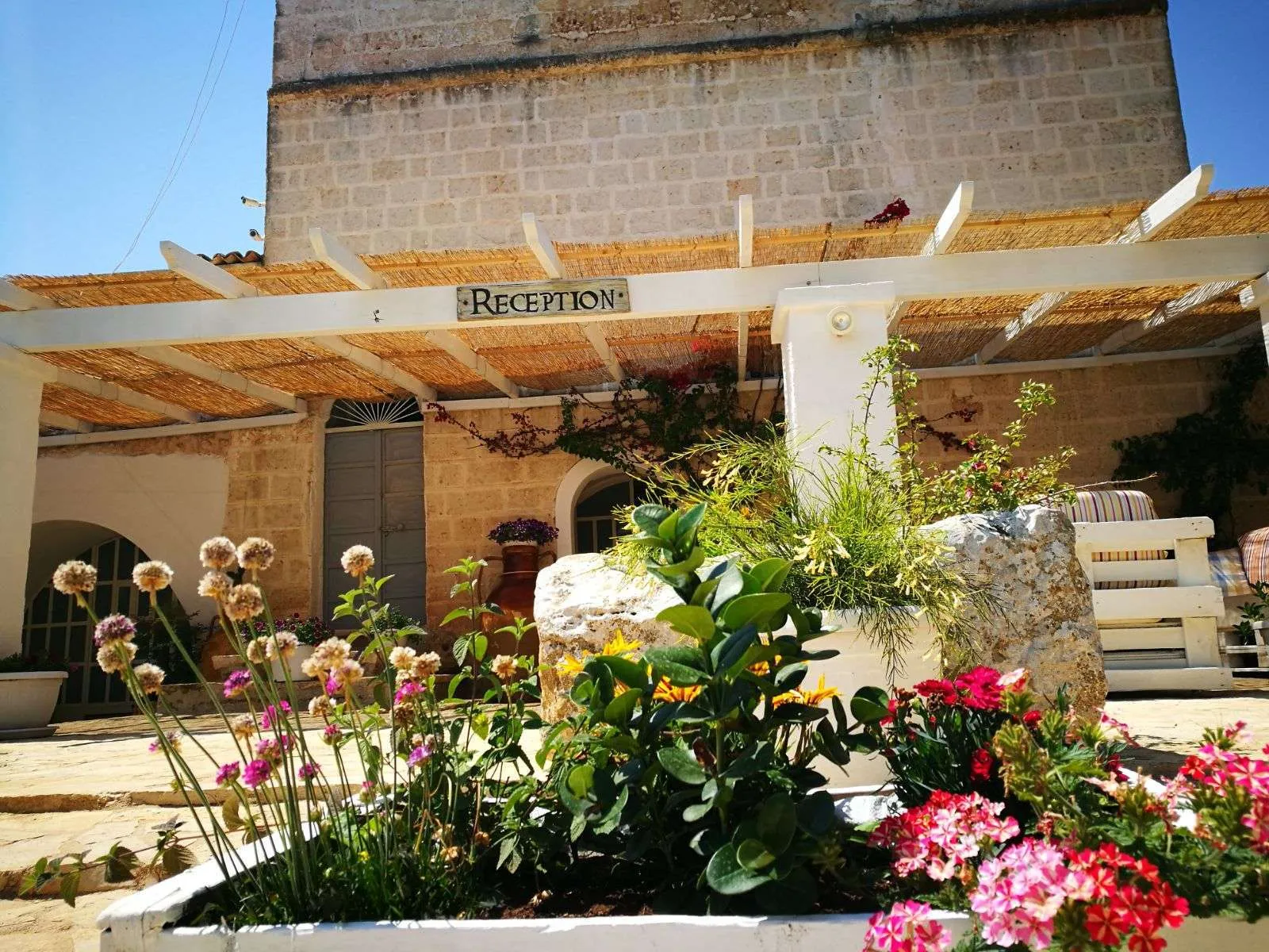 Reception con pergolato in canne, fiori colorati e facciata in pietra
