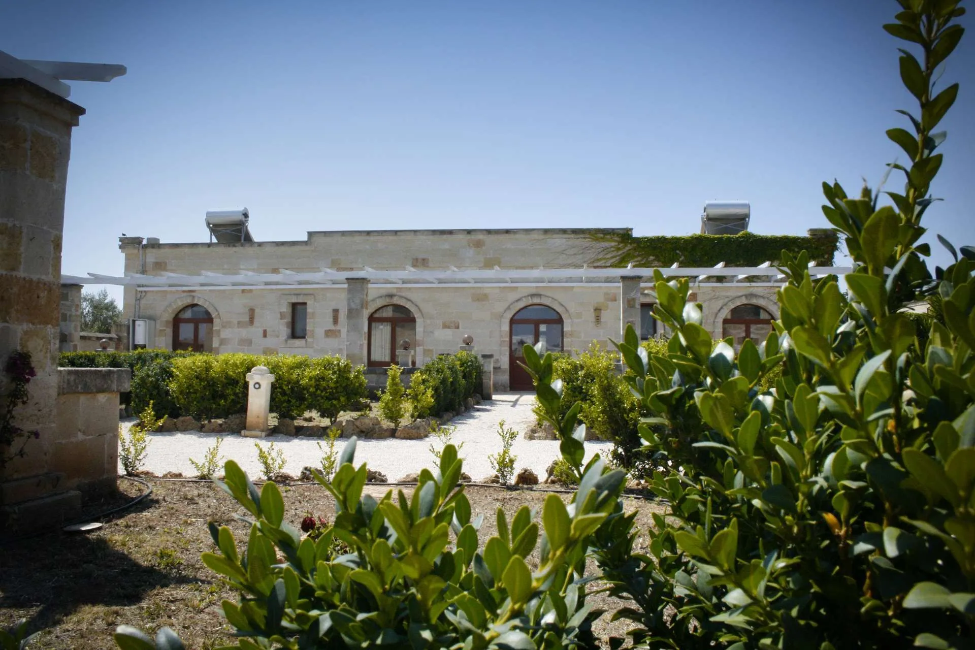 Facciata in pietra con archi, pergolato bianco e giardino curato