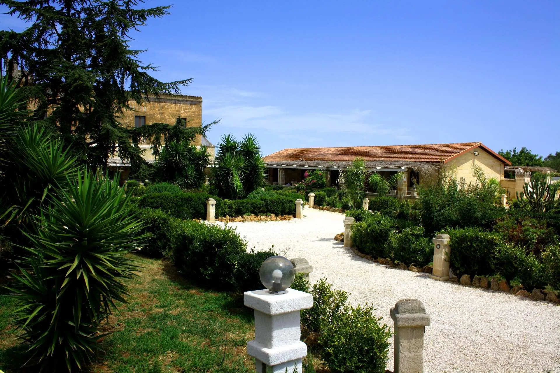 Giardino con piante mediterranee e vialetto verso gli edifici in pietra