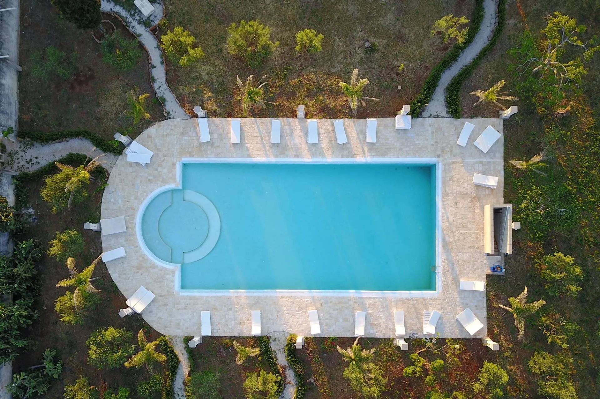 Piscina rettangolare vista dall'alto con lettini bianchi e giardino