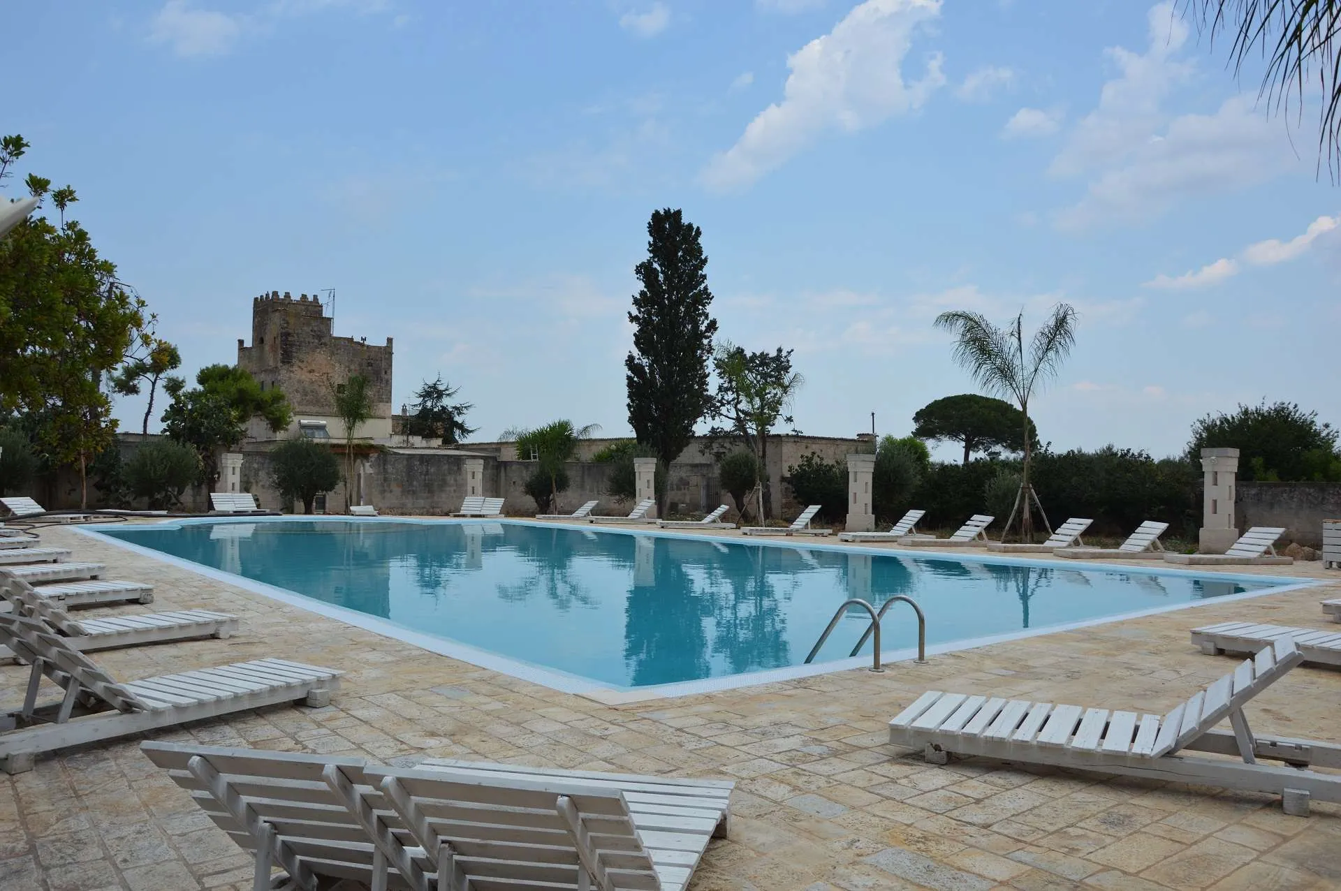 Ampia piscina con lettini bianchi e vista sulla torre della masseria