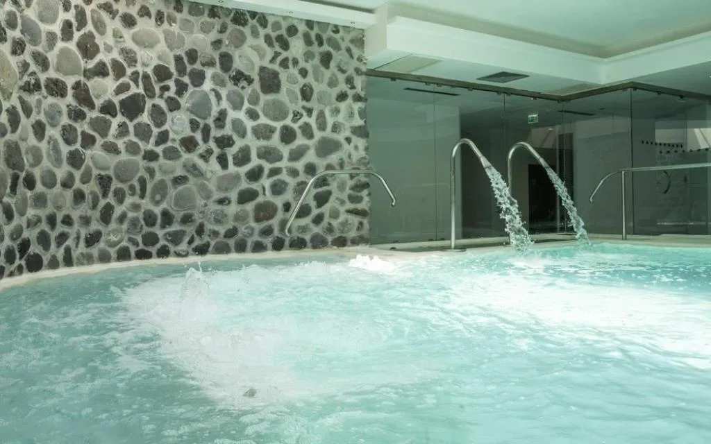 Vasca idromassaggio interna della spa con parete in ciottoli di pietra e getti d'acqua