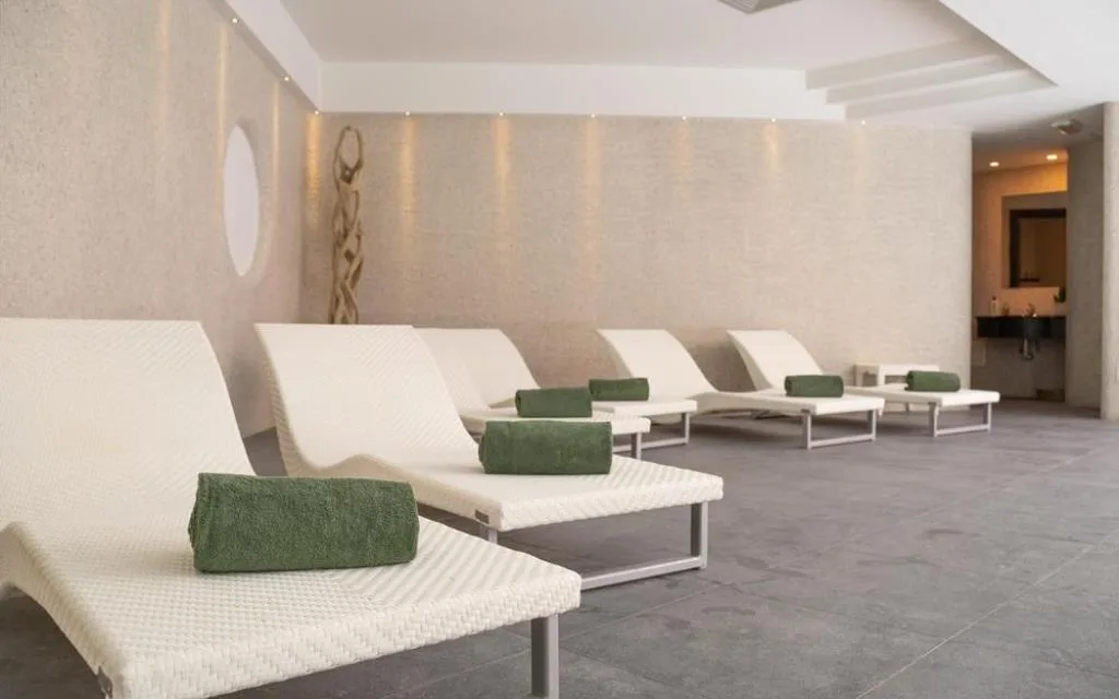 Zona relax della spa con lettini bianchi e asciugamani verdi in ambiente minimalista
