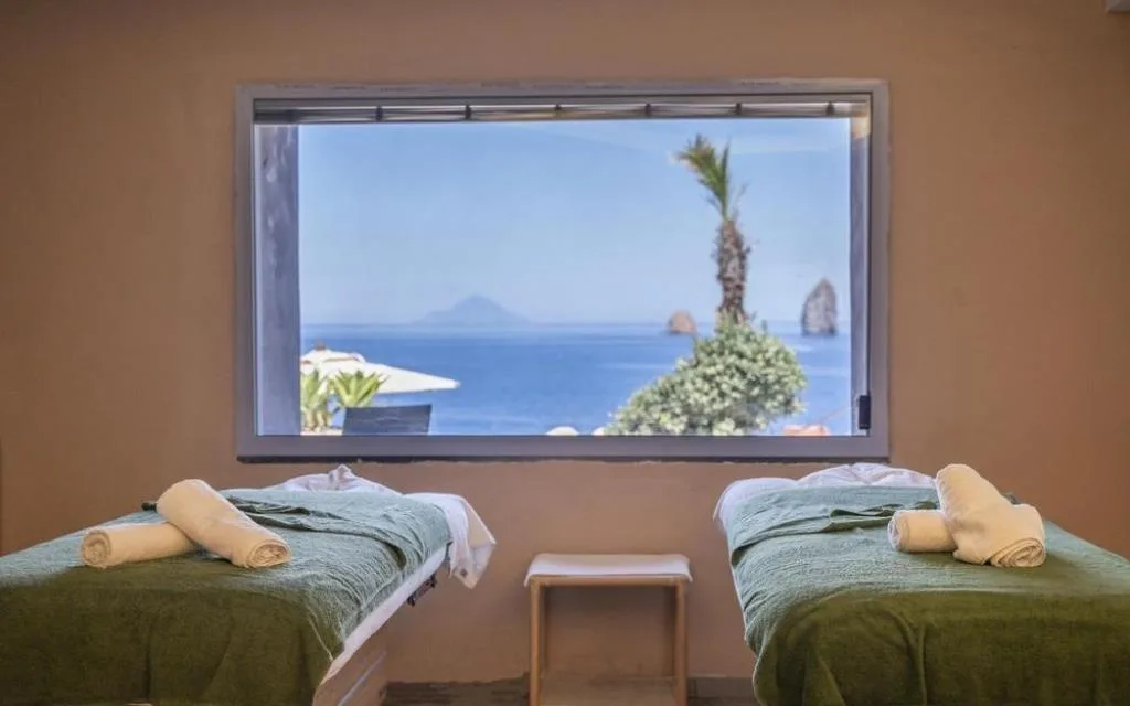 Sala massaggi con due lettini e finestra panoramica sul mare e il vulcano