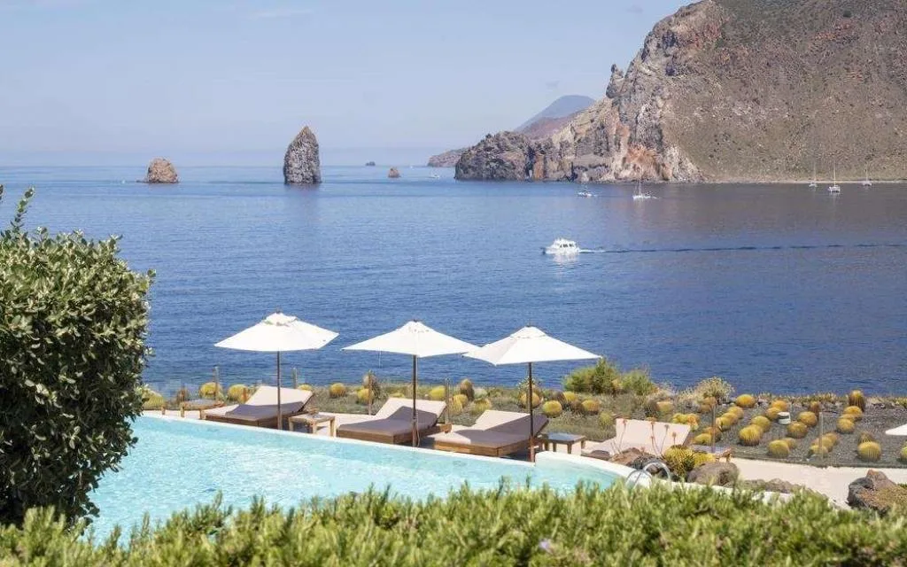 Piscina a sfioro con lettini e ombrelloni e vista sui faraglioni e la scogliera