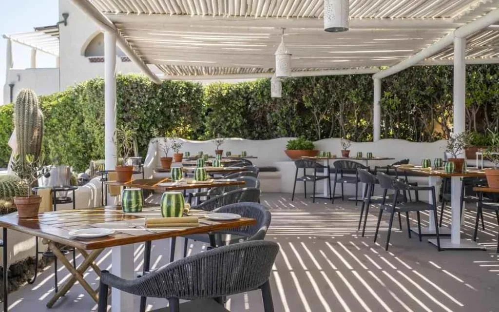 Ristorante all'aperto con pergolato, tavoli in legno e siepe verde