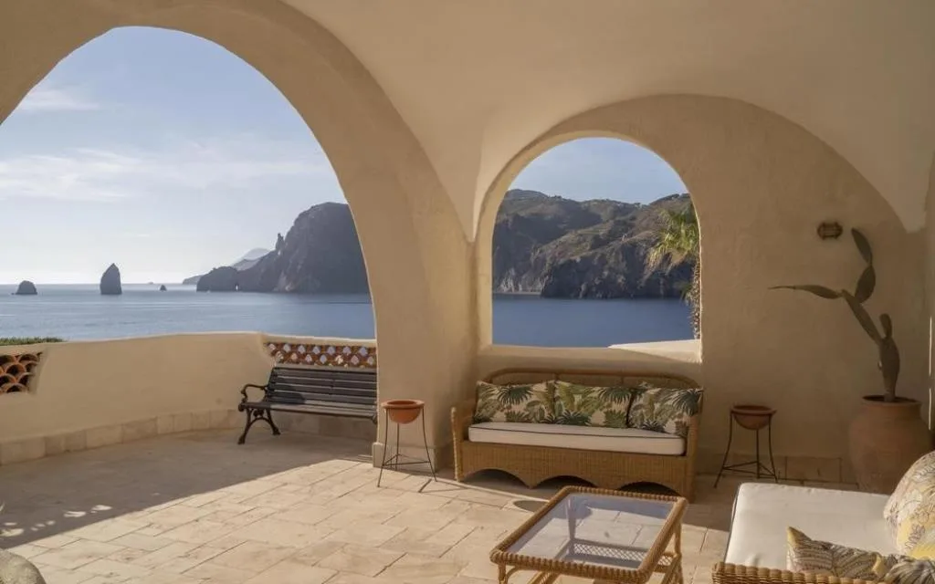Terrazza con archi in muratura, divani in vimini e vista sui faraglioni e la costa