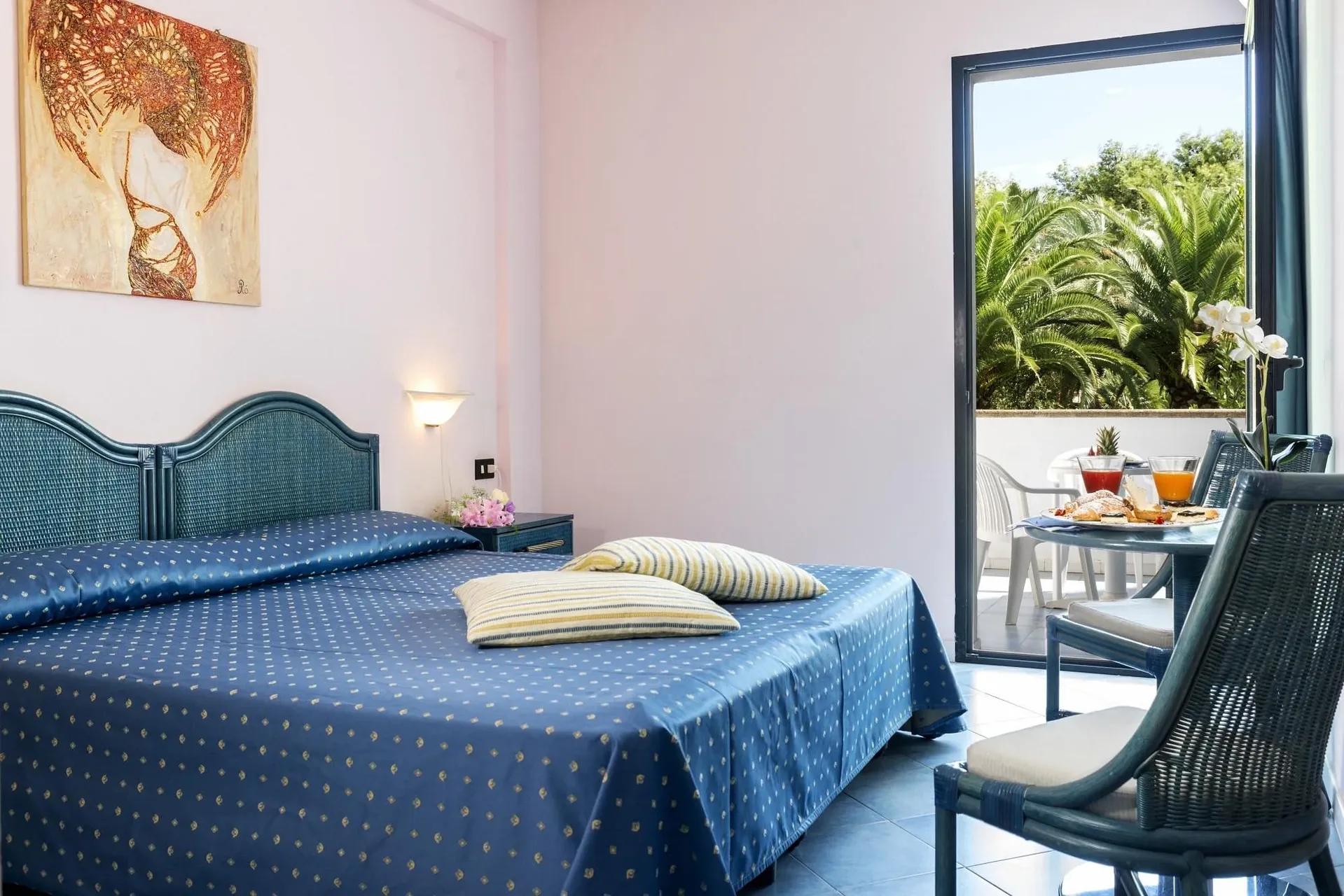 Camera luminosa con letto matrimoniale blu e balcone con colazione vista palme