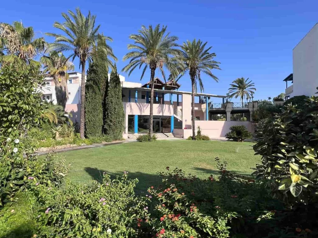Giardino curato con palme alte, prato verde e edificio dell'hotel sullo sfondo