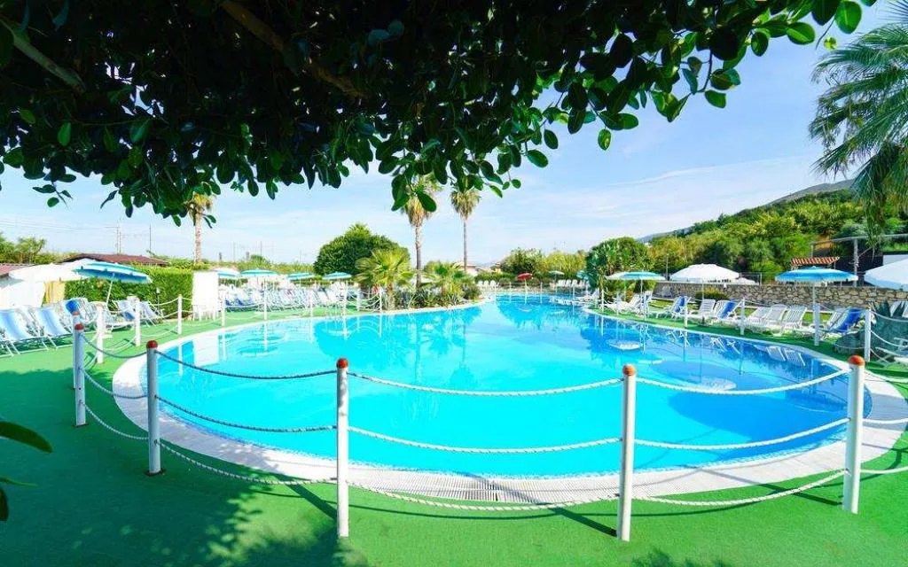 Piscina dalle acque cristalline con lettini, ombrelloni e palme sullo sfondo