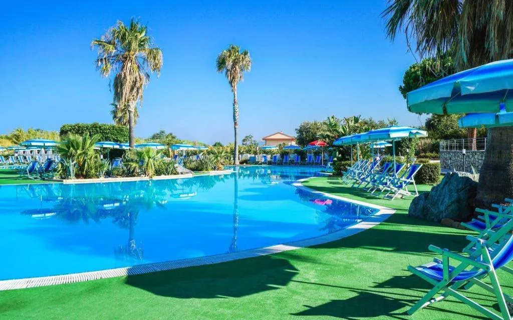 Piscina con palme, lettini e ombrelloni azzurri sotto un cielo sereno
