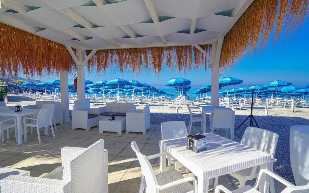 Bar sulla spiaggia con arredi bianchi e vista sugli ombrelloni azzurri e il mare
