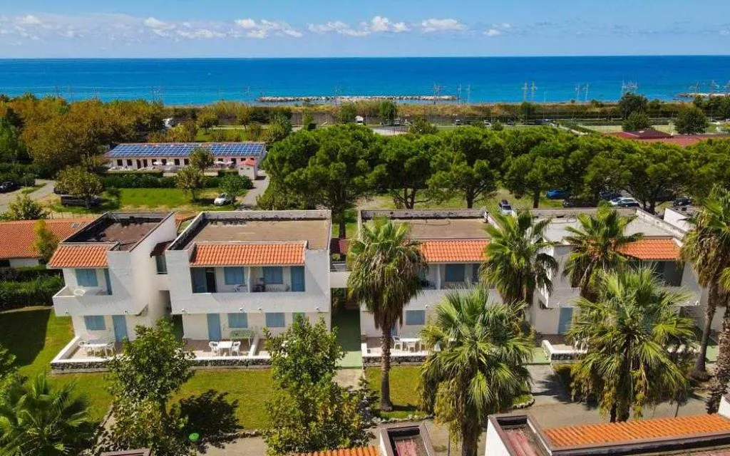 Vista aerea degli alloggi con giardino, palme e il mare sullo sfondo