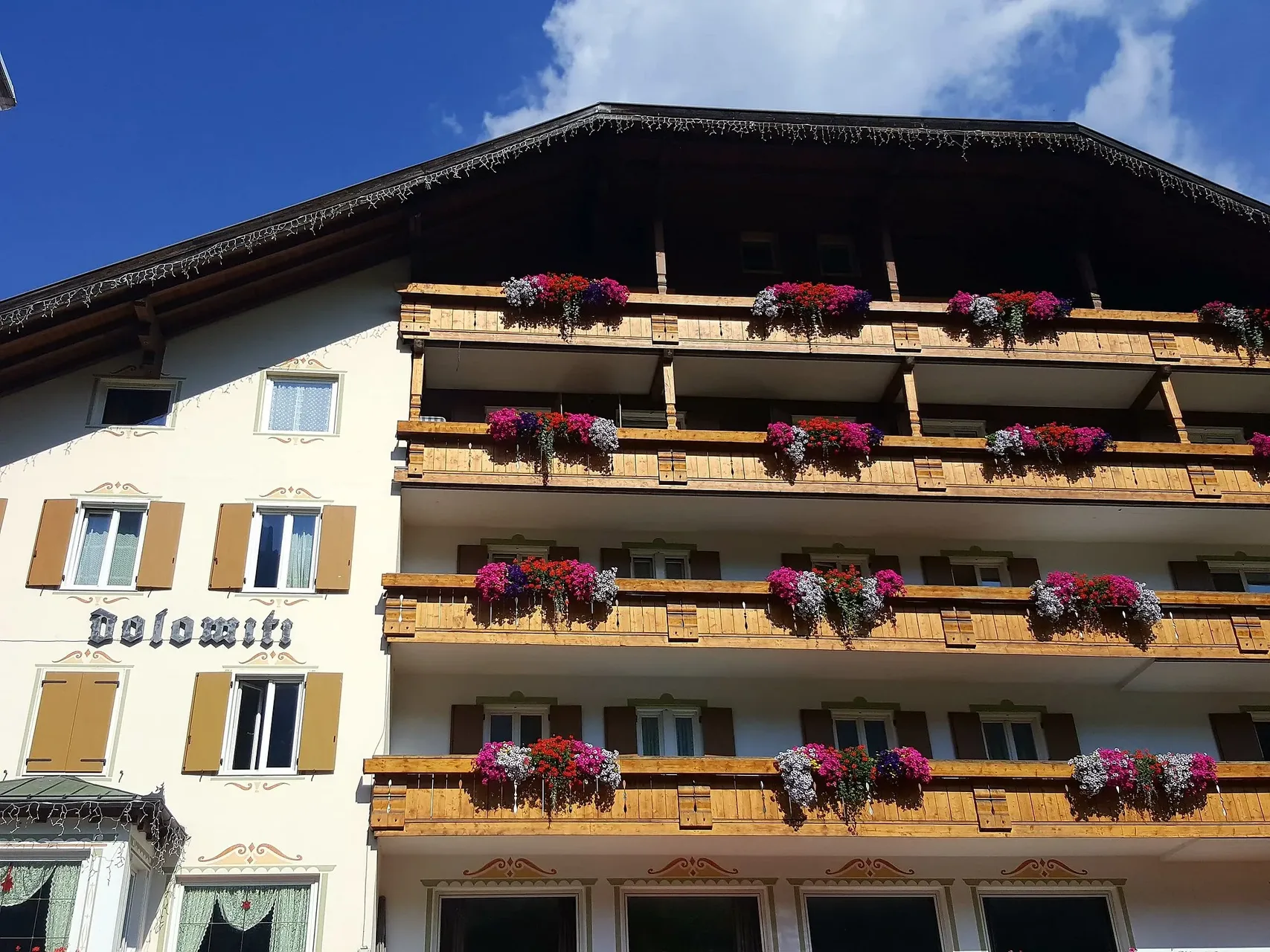 Facciata laterale dell'Hotel Dolomiti con balconi in legno ricchi di fiori colorati