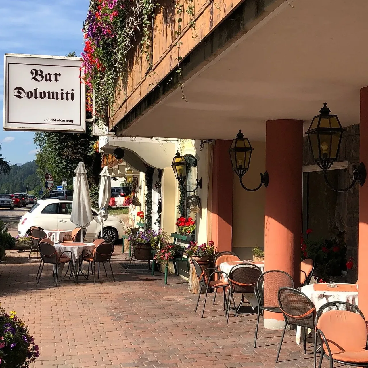 Terrazza esterna del Bar Dolomiti con tavolini, sedie e insegna sotto i portici