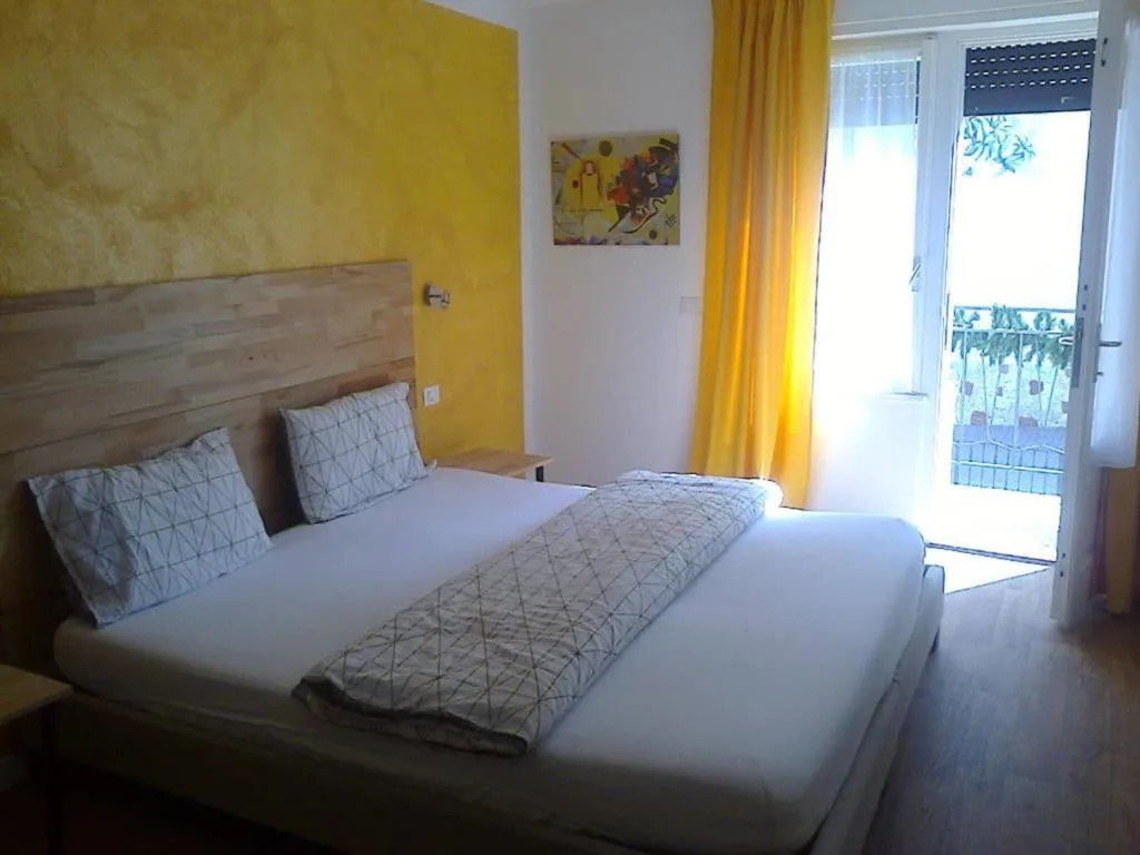 Camera moderna con letto matrimoniale, parete gialla e porta finestra su balcone