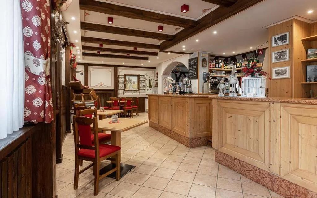 Bar dell'hotel con bancone in legno chiaro, sgabelli e arredo in stile alpino