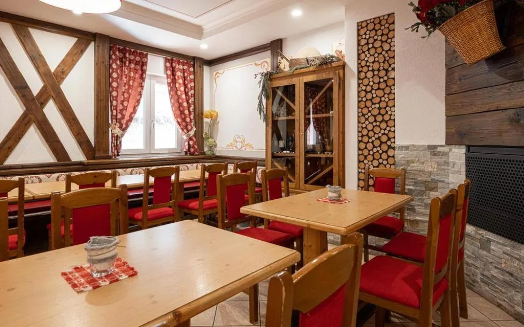 Sala da pranzo rustica con tavoli in legno, sedie rosse e travi a vista