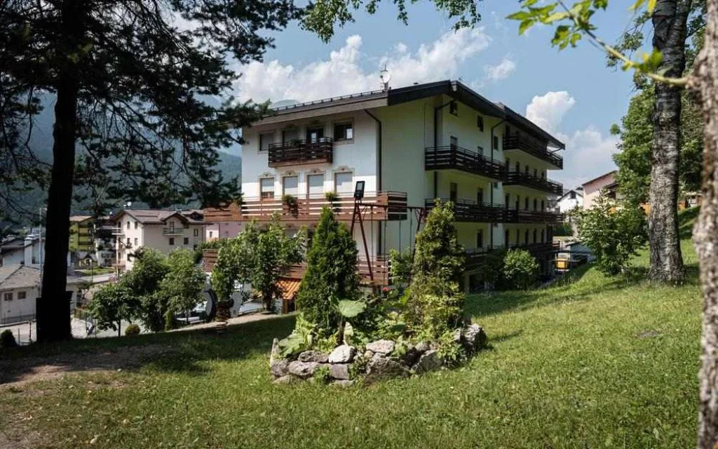 Vista esterna estiva dell'hotel immerso nel verde con giardino e alberi