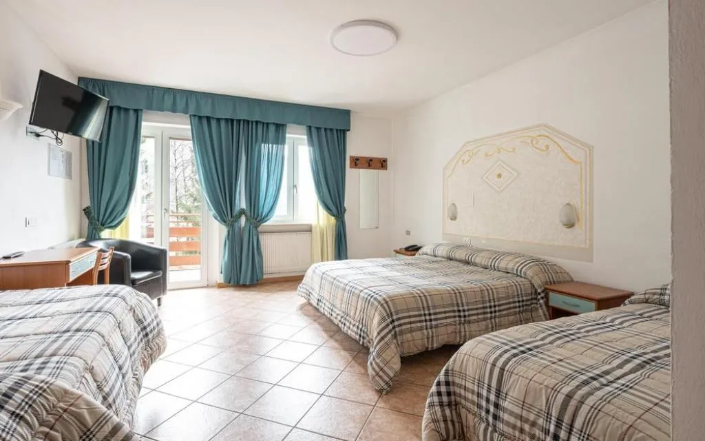 Camera tripla luminosa con tre letti, tende azzurre, TV e testiera decorata