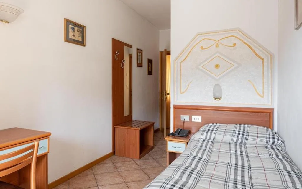 Camera singola con letto, scrivania, appendiabiti e testiera decorata